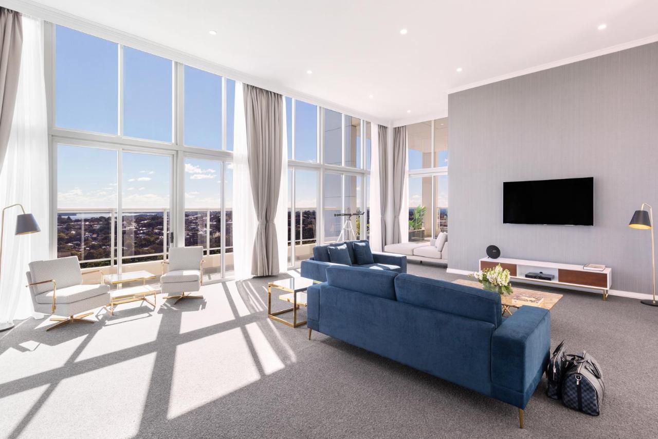 Meriton Suites Bondi Junction Σίδνεϊ Εξωτερικό φωτογραφία The photo shows a bright and modern living room with large floor-to-ceiling windows that provide a view of the outdoors. The space features a blue sofa in the center, complemented by light-colored armchairs nearby. There are light curtains hanging by