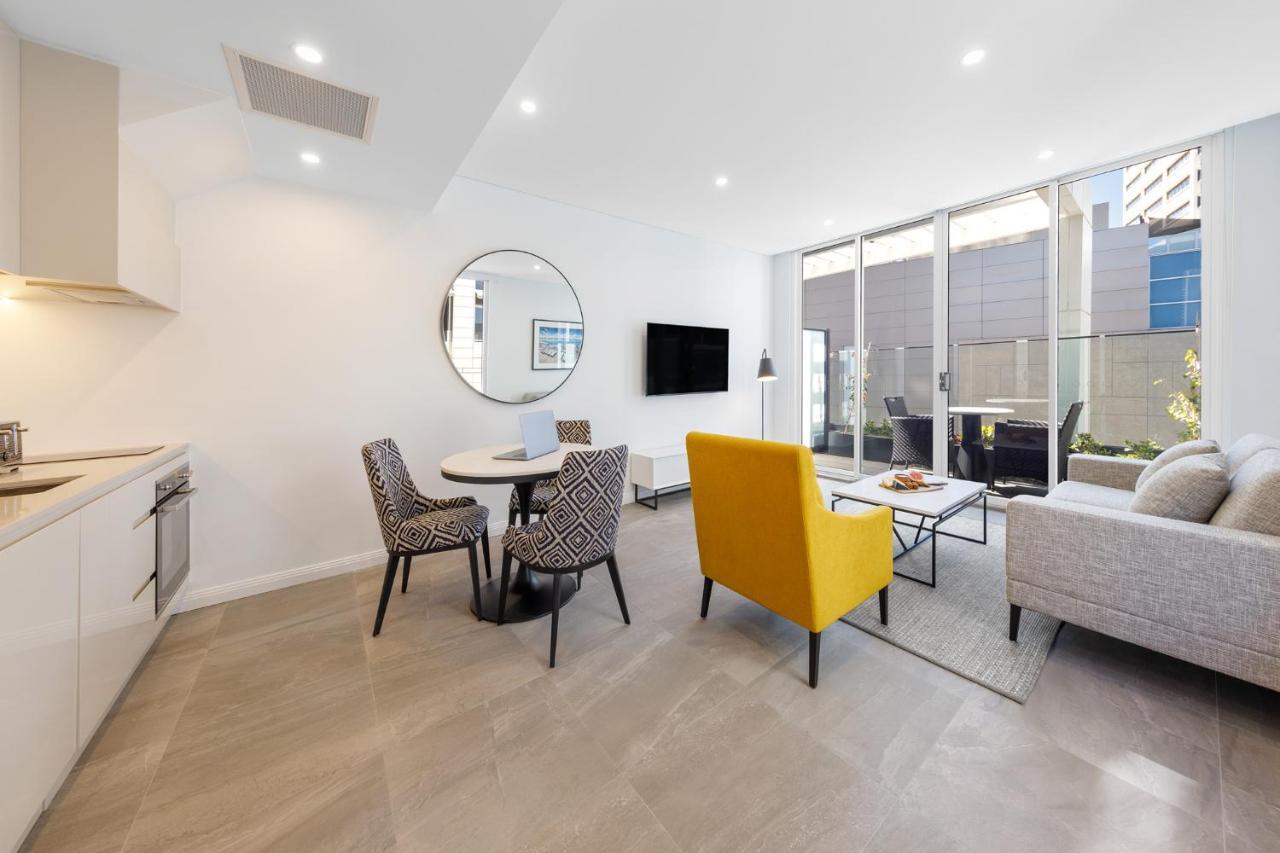 Meriton Suites Bondi Junction Σίδνεϊ Εξωτερικό φωτογραφία The photo shows a modern and stylish living space. On one side, there is a kitchen area with sleek cabinetry, and next to it, a round dining table surrounded by three patterned chairs. In the center of the room, there is a gray sofa accompanied by a 