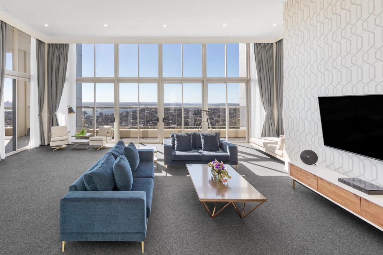 Meriton Suites Bondi Junction Σίδνεϊ Εξωτερικό φωτογραφία The photo shows a modern and spacious living area. It features large windows that provide a panoramic view of the outside landscape and allow natural light to fill the room. The interior design includes a blue sectional sofa placed in the center, com