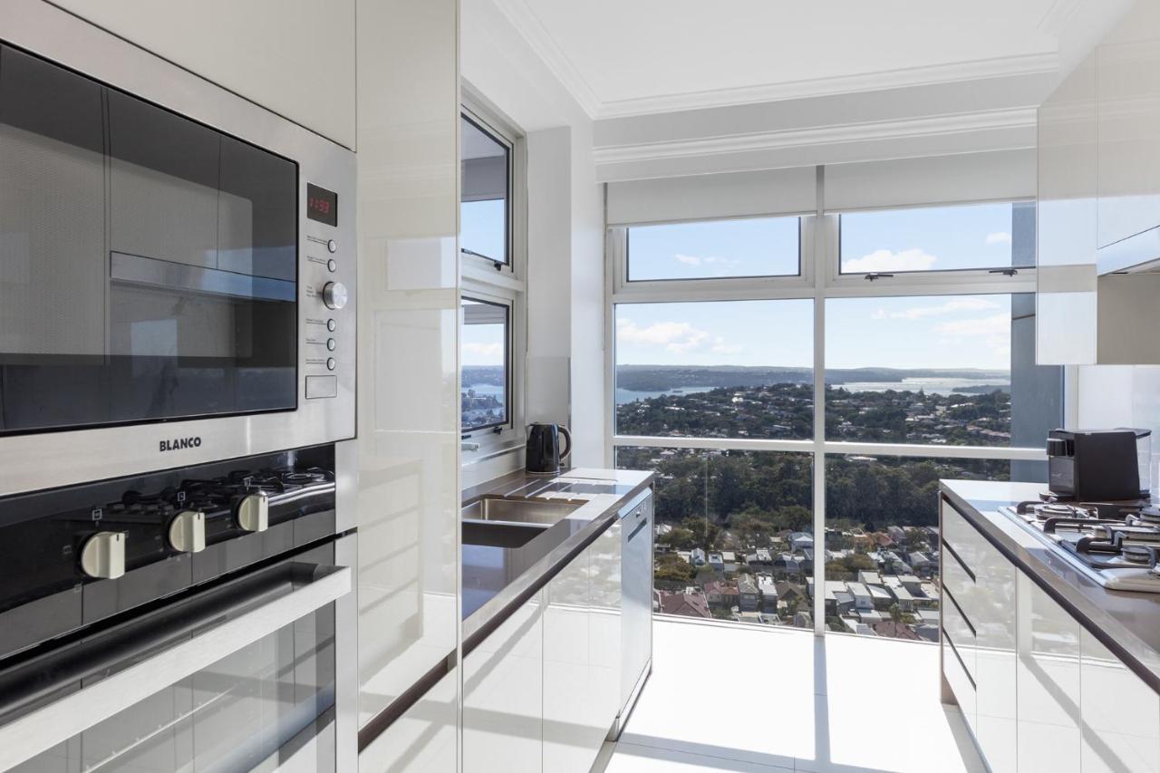 Meriton Suites Bondi Junction Σίδνεϊ Εξωτερικό φωτογραφία The photo shows a modern kitchen with sleek, shiny white cabinets and a large window that offers a panoramic view of the outside landscape. The kitchen features built-in appliances, including an oven and a stove, with a stylish countertop. The spacio