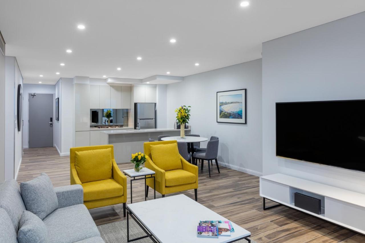 Meriton Suites Bondi Junction Σίδνεϊ Εξωτερικό φωτογραφία The photo shows a modern living space that includes a cozy sitting area and a dining area. The sitting area features two bright yellow chairs and a light gray sofa, arranged around a coffee table. There are decorative items on the table, including fl