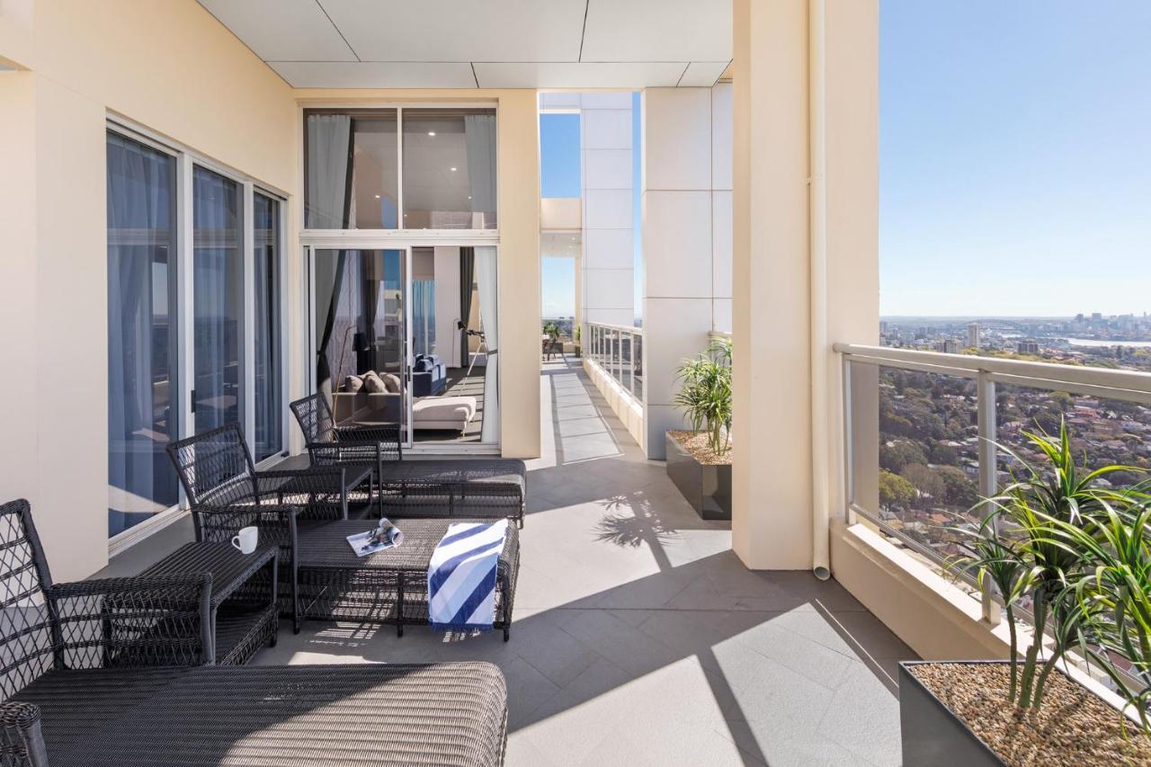 Meriton Suites Bondi Junction Σίδνεϊ Εξωτερικό φωτογραφία The photo shows a spacious balcony or terrace area of a high-rise building. It features modern outdoor furniture, including a seating arrangement with dark wicker chairs and a table. There are cushions, and a blue and white striped blanket is draped 