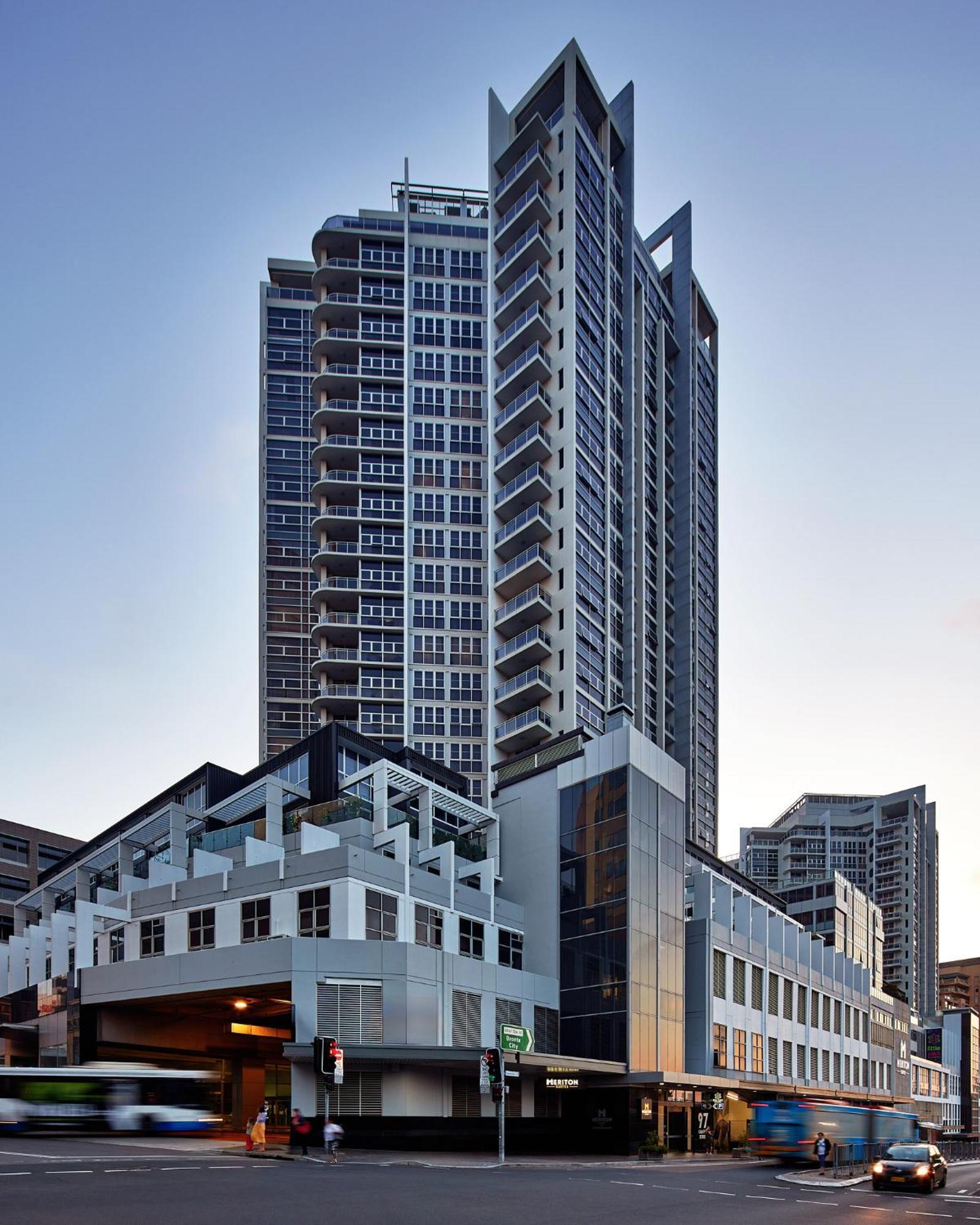 Meriton Suites Bondi Junction Σίδνεϊ Εξωτερικό φωτογραφία The image shows a modern high-rise building with a sleek design. The structure features a mix of glass and concrete elements, with multiple levels showcasing balconies. The building appears to be part of an urban environment, likely containing reside