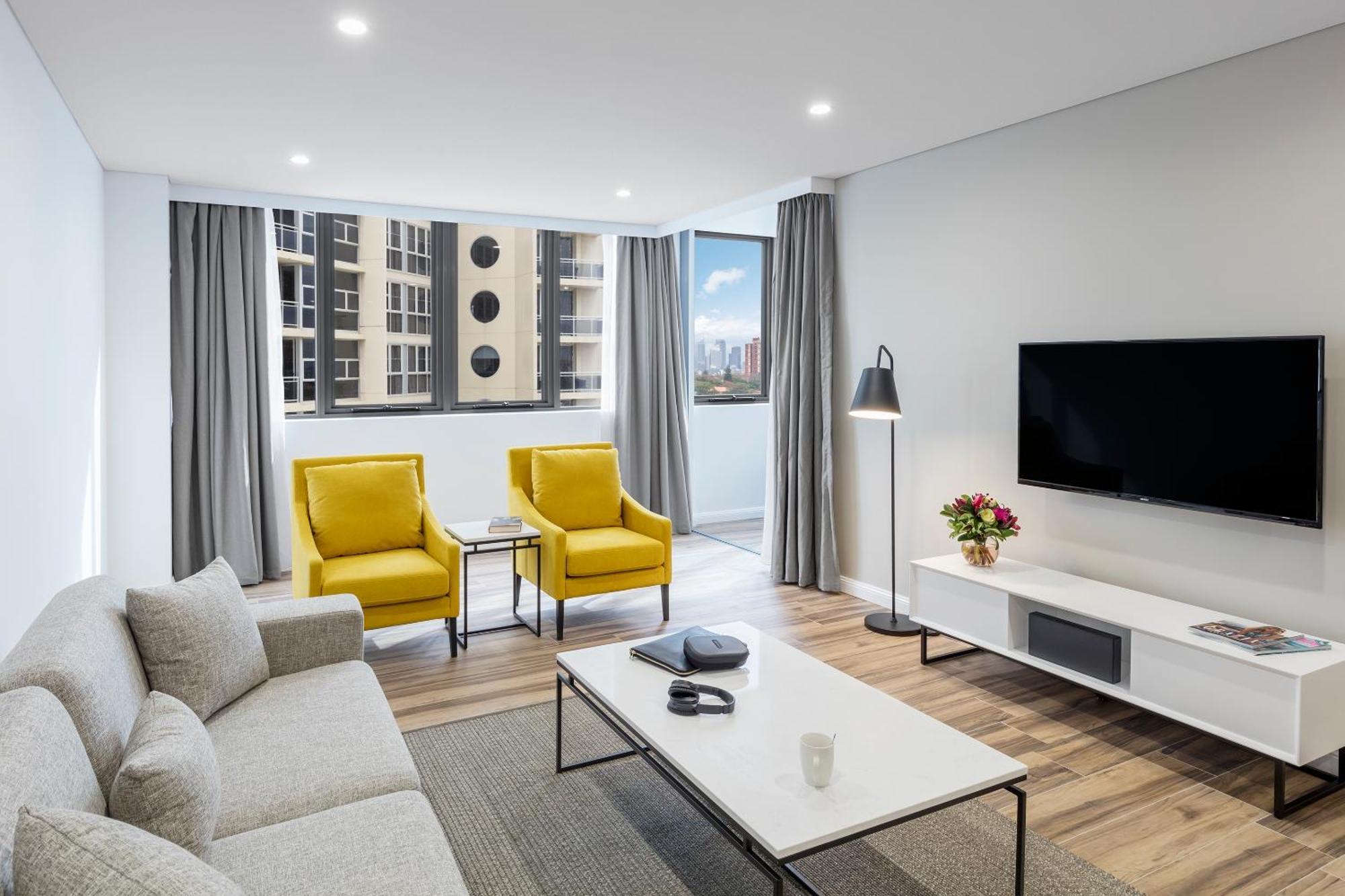 Meriton Suites Bondi Junction Σίδνεϊ Εξωτερικό φωτογραφία The photo shows a modern, well-lit living room. It features a light gray sofa with a textured fabric. There are two bright yellow armchairs positioned near a window, which allows natural light to enter the space. The room has light gray curtains and 